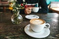 Two cups of coffee and a vase of flowers on a wooden table, the man holds in her hand one cup of coffee in the Royalty Free Stock Photo