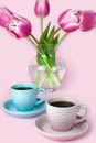Two cups of coffee and a vase with pink tulips on the pink background. Copy space. Close-up Royalty Free Stock Photo