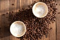 Two cups of fresh black coffee or espresso in eco-friendly cups on a wooden table and coffee beans scattered side by side.