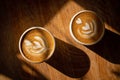 Two cups of fresh cappuccino with latte art on brown wooden table and long deep shadows. Coffee break in cafe. Delicious Royalty Free Stock Photo