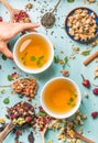 Two cups of healthy herbal tea with mint, cinnamon, dried rose and camomile flowers in different spoons, woman`s hand Royalty Free Stock Photo