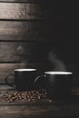 Two cups of hot coffee with steam and coffee beans on a wooden and black background. hot drink Royalty Free Stock Photo