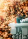 Two cups of hot tea or coffee stand on the balcony parapet against the backdrop of autumn trees.