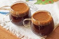 Two cups of tasty coffee with foam, on a wooden table covered with a colored textile material