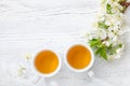 Two cups of tea and branch of blossom cherry on white wooden table