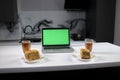 Two cups of tea and two pieces of cake in gray kitchen next to laptop with green screen - chromakey Royalty Free Stock Photo