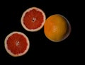 Two cut halves bright red orange grapefruit and whole fruit on black backdrop Royalty Free Stock Photo