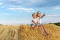 Two cute adorable caucasian siblings enjoy having fun sitting on top over golden hay bale on wheat harvested field near farm.