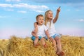 Two cute adorable caucasian siblings enjoy having fun sitting on top over golden hay bale on wheat harvested field near