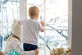 Two cute adorable little blond cauasian children siblings stay near window and looking outside waiting for snow, wonders