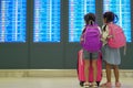 Two asian child girls with backpack checking their flight at information board in international airport terminal