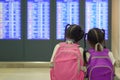 Two asian child girls with backpack checking their flight at information board in international airport terminal