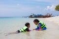 Two asian child girls wearing life jacket playing water in the beautiful sea together with fun in summer vacation Royalty Free Stock Photo