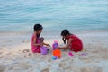 Two asian little child girls sitting and playing with sand together on the beach near the beautiful sea in summer vacation Royalty Free Stock Photo