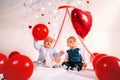 Two cute babies in fancy clothes, posing with red balloons. Bright room decorated with hearts and balloons. Valentine`s day Royalty Free Stock Photo