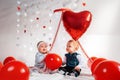 Two cute babies in fancy clothes, posing with red balloons. The concept of Valentine`s day and romance Royalty Free Stock Photo