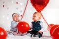 Two cute babies in fancy clothes, posing with red balloons. The concept of Valentine& x27;s day and romance Royalty Free Stock Photo