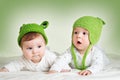 Two cute babies lying in frog hats on spft blanket