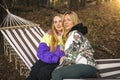 Two cute blonde women sitting in the hammock and laughing in the sunny forest