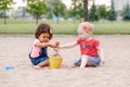 Two cute Caucasian and hispanic latin toddlers babies children sitting in sandbox playing with plastic colorful toys