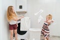 two cute and cheerful girls play with laundry in the laundry room.