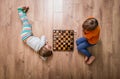 Two cute children playing chess at home while lying on floor. Boy and girl. Win and lost game. Win win.