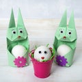 Two cute Easter bunny egg holders and an egg with a face in a bucket. Easter concept. Rabbits are made in origami technique Royalty Free Stock Photo