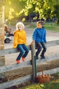 Two cute funny Caucasian children boy girl sitting on wooden rustic fence in park farm outside. Friends siblings kids talking at Royalty Free Stock Photo