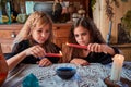 Two cute girls aged 10 years in witch costumes in an old house on Halloween dripping candle wax in blue water and conjuring.