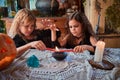 Two cute girls aged 10 years in witch costumes in an old house on Halloween dripping candle wax in blue water and conjuring.