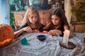 Two cute girls aged 10 years in witch costumes in an old house on Halloween dripping candle wax in blue water and conjuring.