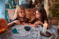 Two cute girls aged 10 years in witch costumes in an old house on Halloween dripping candle wax in blue water and conjuring.