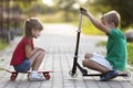 Two cute happy funny smiling young children, brother and sister, posing for camera, handsome boy with scooter and pretty long- Royalty Free Stock Photo