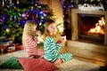 Two cute happy girls having hot chocolate by a fireplace in a cozy dark living room on Christmas eve.