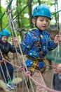 Two cute happy young children, boy and girl in protective harness, carbine and safety helmets on rope way on bright sunny day on