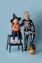 Two cute kids, boy and girl wearing witch and skeleton costumes over blue