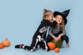 Two cute kids in witch and skeleton costumes gossiping over blue background Royalty Free Stock Photo