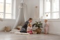 Two cute little baby girls play with their mom in a bright minimalistic children`s room.