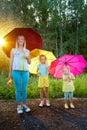 Two cute little blonde girls sisters and mother with umbrellas under rain drops in a summer sunny day. Happy family Royalty Free Stock Photo