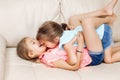 Two cute little Caucasian girls siblings playing at home. Adorable children kids lying hugging on a couch together. Authentic Royalty Free Stock Photo