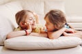 Two cute little Caucasian girls siblings playing at home. Adorable smiling children kids lying on a couch together. Authentic