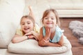 Two cute little Caucasian girls siblings playing at home. Adorable smiling children kids lying on a couch together. Authentic Royalty Free Stock Photo