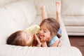 Two cute little Caucasian girls siblings playing at home. Adorable smiling children kids lying on a couch together. Authentic Royalty Free Stock Photo