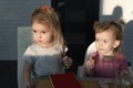 Two cute little caucasian girls sitting at the table, eating, looking.