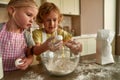 Two cute little children, boy and girl in aprons adding eggs while preparing dough together on the kitchen table at home Royalty Free Stock Photo