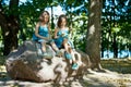 Two cute little girls in dresses sit on a stone and drink lemonade