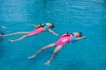 Two cute little girls in life jackets having fun swimming in the pool. Cute sisters practicing floating in the pool. Summer