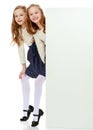 Two little girls peeking out from behind a white advertising ban Royalty Free Stock Photo