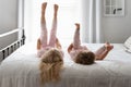 Two cute little girls lying on a big white bed with their feet in the air Royalty Free Stock Photo