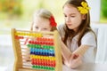 Two cute little girls playing with abacus at home. Big sister teaching her sibling to count. Smart child learning to count.